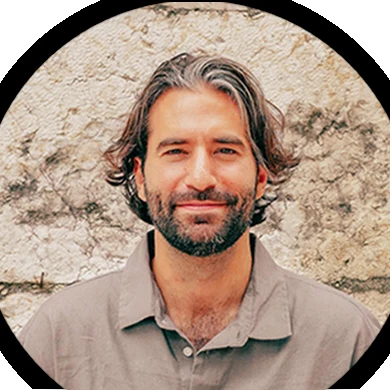 Portrait of Malek Najm Ghaleb, founder of Alchemist Ways, smiling in front of a stone wall.